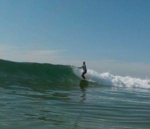 Surfista montando una ola, manteniendo el equilibrio sobre una tabla de surf en medio del agua del mar, bajo un cielo azul claro.