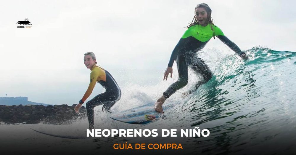 Dos niños surfeando una ola, vestidos con trajes de neopreno verdes y amarillos, con una costa rocosa y colinas lejanas al fondo. Texto: "Blog de CORE Surfing - Neoprenos de Niño - Guía de Compra."