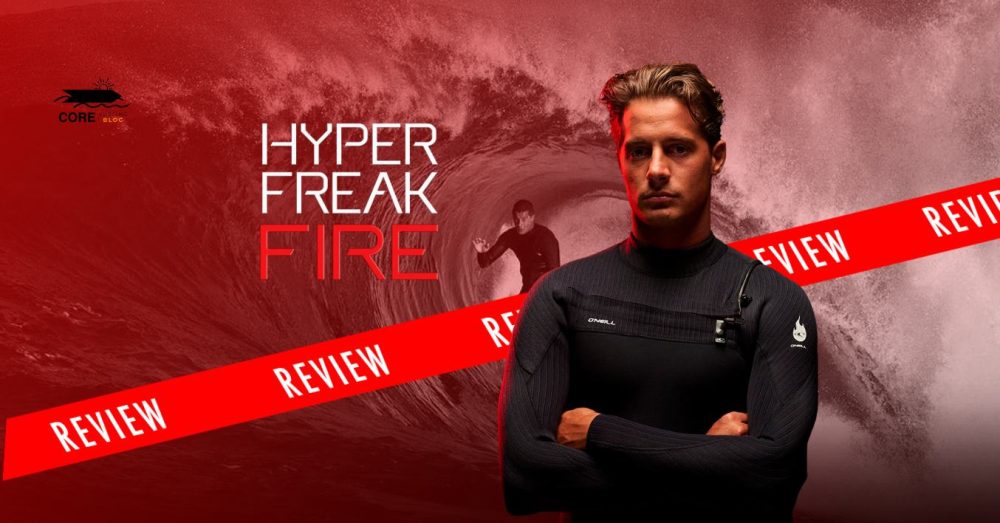 Un hombre vestido con un traje de neopreno negro se encuentra con los brazos cruzados frente a una gran ola, mientras otra persona surfea al fondo. El texto lee: "HYPER FREAK FIRE REVIEW."