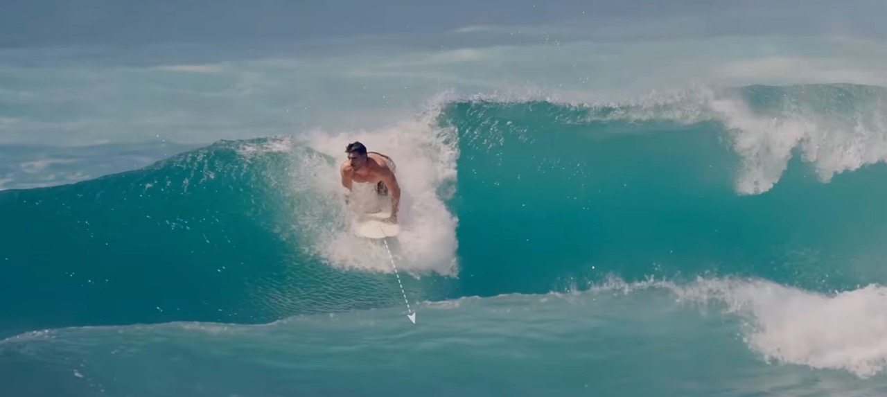 Surfista remando recto hacia la playa para asegurar la entrada en una ola lenta