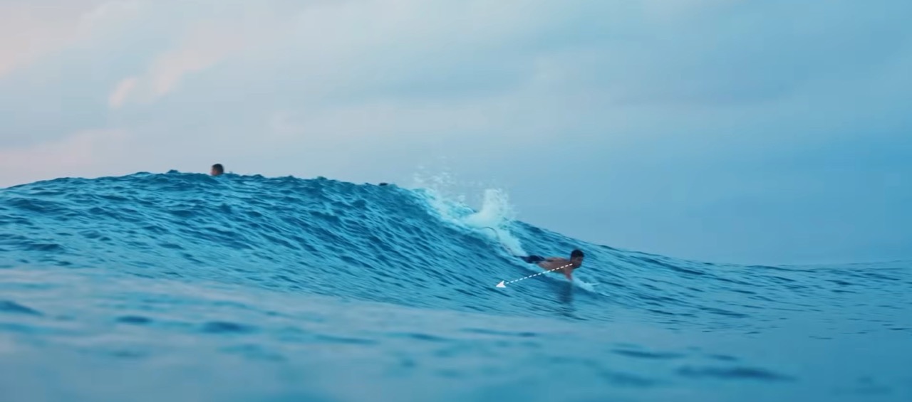 Surfista remando con la mirada puesta en la parte alta de la pared para leer la ola